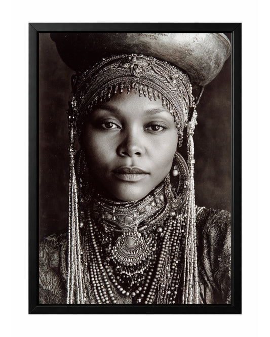 Monochrome African-inspired woman portrait with ornate head covering, layered jewelry, and vessel above her head.